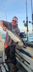 Angler proudly displaying a large Salmon aboard a fishing boat, showcasing a successful day on the water.
