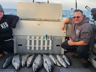 Two anglers proudly posing next to a display of freshly caught salmon on a fishing charter.