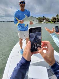A proud angler displaying a large Jack Crevalle while friends capture the moment on their phones during a fishing trip.