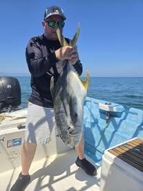 Angler proudly displaying a large Jack Crevalle while fishing on a sunny day in open waters.