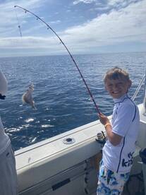 A young angler joyfully reeling in a fish while fishing on a boat in open waters, showcasing the excitement of the catch.