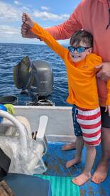 A young angler proudly displaying a caught fish while fishing on a boat, showcasing a fun family outing.