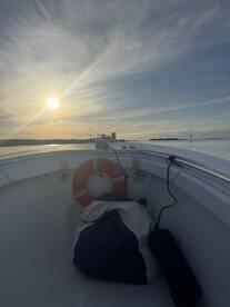 A serene view from the interior of a boat, showcasing a life ring and a bag, with a beautiful sunset over the water.