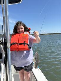 A young angler proudly holding a fish while fishing on a sunny day, showcasing a fun family outing on the water.