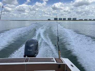 A scenic view from the back of a boat, showcasing the powerful Yamaha 300 engine and the calm waters, with buildings lining the shore in the background.