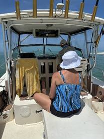 Interior view of a fishing boat showing a woman seated in a colorful top, with a captain at the helm, navigating through calm waters.
