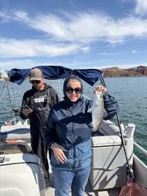 A proud angler displaying a freshly caught striped bass while fishing on a boat, with a scenic backdrop of hills and clear skies.
