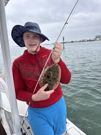 A young angler proudly displaying a caught Flounder while fishing from a boat in a coastal waterway.