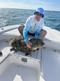 Angler proudly displaying a large Grouper on the deck of a boat during a fishing trip.