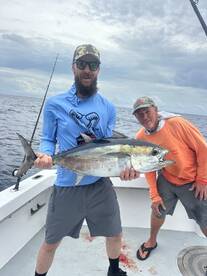 Two anglers proudly displaying a large Yellowfin Tuna on a fishing charter in open waters.