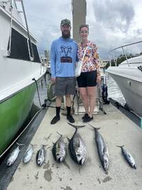 Two anglers proudly standing by their catch of various tuna species displayed on the dock after a successful fishing trip.