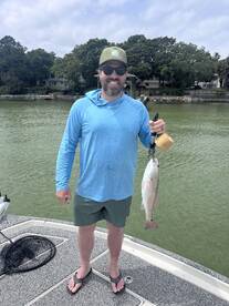 Angler proudly displaying a freshly caught Redfish while standing on the boat in a scenic waterway.