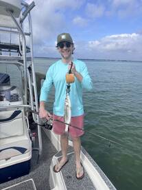 Angler proudly displaying a Speckled Trout while fishing from a boat in a coastal waterway.