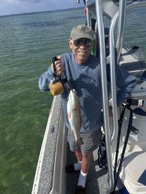 A proud angler holding a freshly caught Redfish while standing on a boat in clear waters.