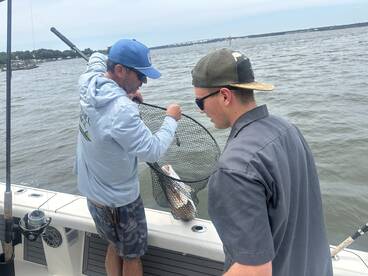 Two anglers on a boat working together to land a fish using a net, showcasing teamwork during a fishing trip.