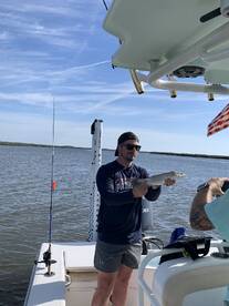 Angler holding a Speckled Trout on a boat in a scenic fishing environment.