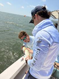 Two anglers actively engaged in catching a Speckled Trout while fishing on a sunny day, showcasing the excitement of the catch.