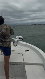 A young angler is actively reeling in a fish while fishing from a Coastline boat, with a cloudy sky in the background.