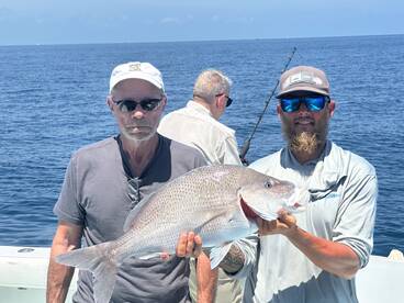 Two anglers proudly displaying a large Snapper while fishing offshore, showcasing a successful day on the water.