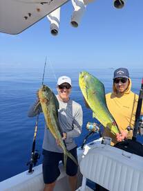 Two anglers proudly displaying their catches of vibrant Mahi Mahi while out on a fishing charter in calm waters.