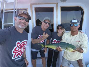 Group of anglers proudly displaying a vibrant Mahi Mahi aboard a fishing charter, showcasing a successful day on the water.