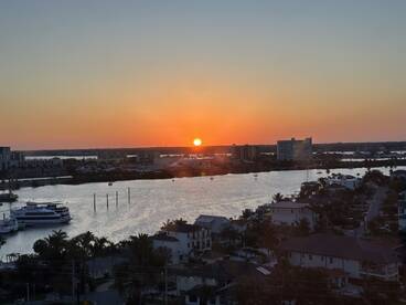 A scenic sunset view over a waterfront area, showcasing boats and buildings along the shore.