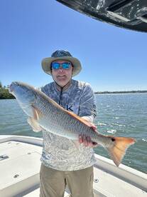 Angler proudly displaying a large Redfish while standing on a boat, enjoying a sunny day on the water.
