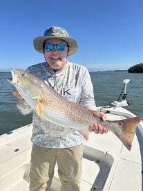 Angler proudly displaying a large Redfish while fishing on a sunny day.
