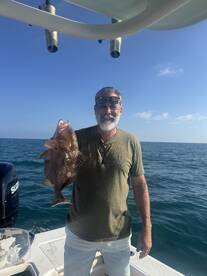 Angler proudly displaying a large Grouper while fishing on a boat in open waters.