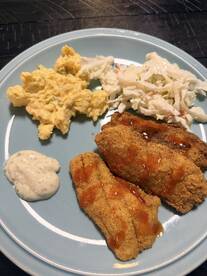 A plate of fried fish fillets served with coleslaw and scrambled eggs, showcasing a delicious meal after a fishing trip.