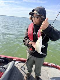 A young angler proudly displaying a freshly caught striped bass while fishing on a boat.