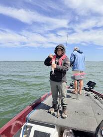 A young angler is focused on reeling in a fish while fishing from a boat in a scenic waterway, showcasing the excitement of the catch.