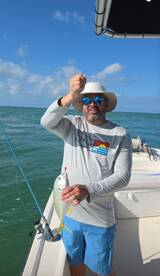 Angler proudly displaying a small fish while fishing on a boat in clear waters.