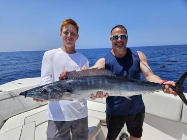 Two anglers proudly displaying a large Wahoo while fishing offshore, showcasing a successful day on the water.