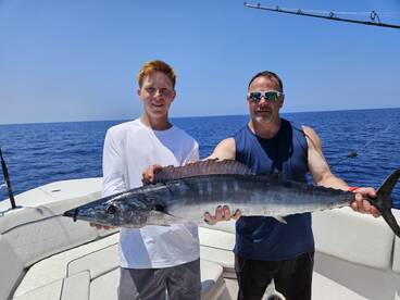 A young angler and an adult proudly display a large Wahoo caught during a deep-sea fishing trip.