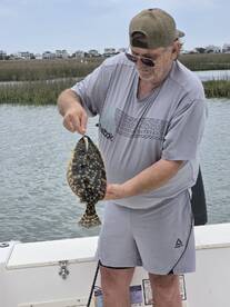 An angler proudly displaying a Flounder while fishing from a boat in a coastal marsh environment.