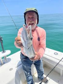 An angler proudly displaying a large Barracuda while fishing on a boat in clear blue waters.