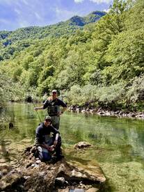 Two anglers fishing in a scenic river surrounded by lush greenery, showcasing a tranquil outdoor experience.