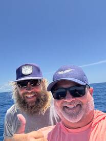 Two anglers enjoying a sunny day on the water, smiling for a selfie while out fishing.