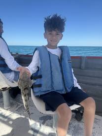 A young angler proudly displaying a caught fish while seated in a boat, enjoying a sunny day on the water.