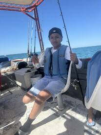 A young angler proudly displaying a small fish while seated on a fishing boat, enjoying a day out on the water.