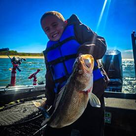 A young angler proudly displaying a large Walleye while fishing on a sunny day, showcasing the excitement of youth fishing adventures.