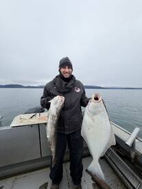 Angler proudly displaying a large Halibut and a Cod while fishing in a scenic coastal environment.