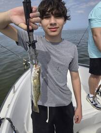 A young angler proudly displaying a Speckled Trout while fishing on a boat, showcasing a successful day on the water.