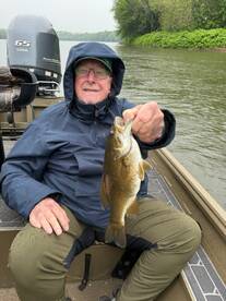 An angler proudly displaying a Smallmouth Bass while fishing on a rainy day in a river setting.