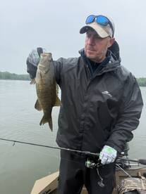 Angler proudly displaying a large Largemouth Bass while fishing on a calm river.