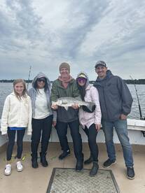 A family proudly displaying a large striped bass on a fishing charter, enjoying a day on the water.