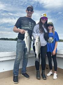 Family proudly displaying their catch of striped bass while enjoying a day on the water.