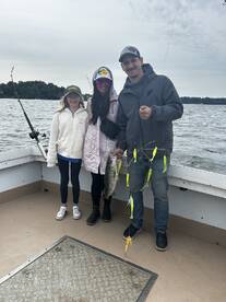 A family enjoying a fishing trip, proudly displaying a striped bass caught on a boat, showcasing a fun day on the water.