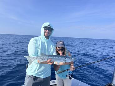 Two anglers proudly displaying a Barracuda while fishing offshore, showcasing a successful day on the water.